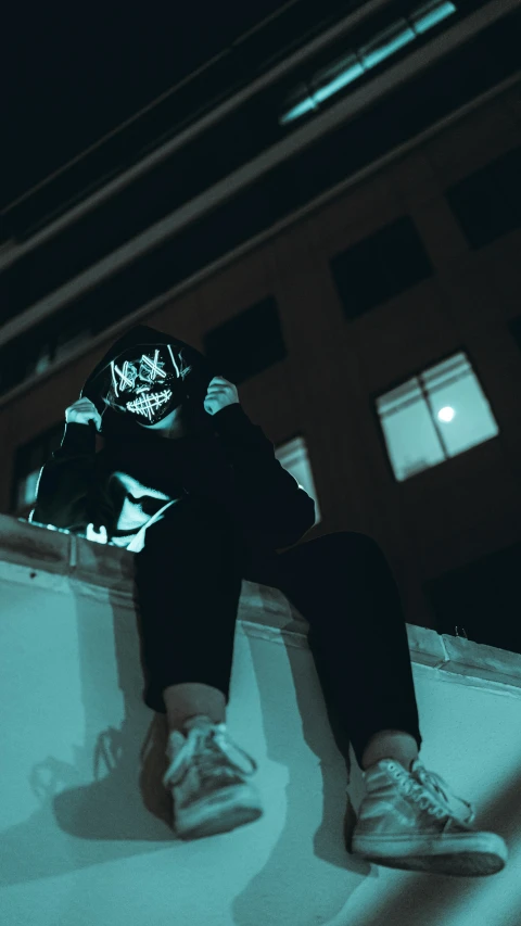 a person in sneakers and jeans is sitting on the edge of a building at night