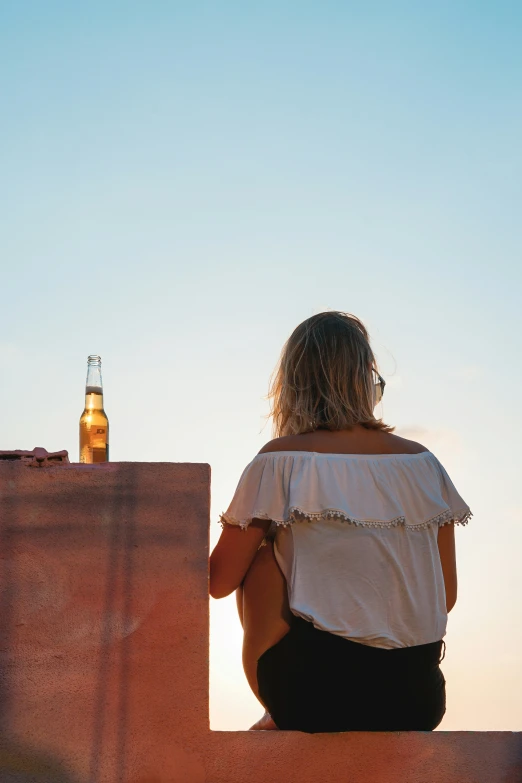 a woman sitting on a brick wall while looking at the sunset