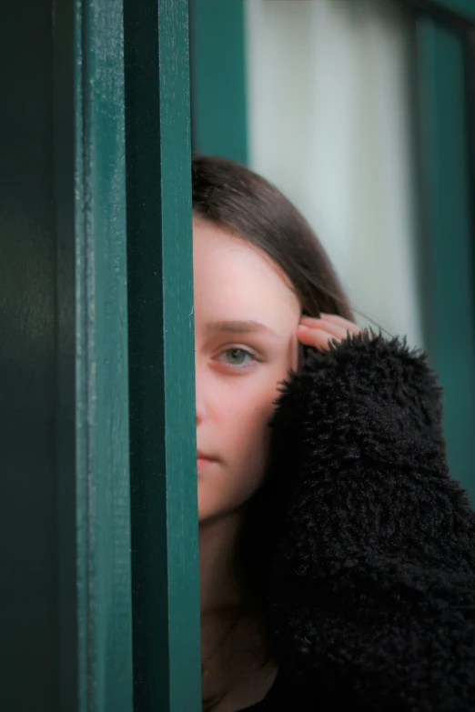 a person looking out the window behind a green curtain