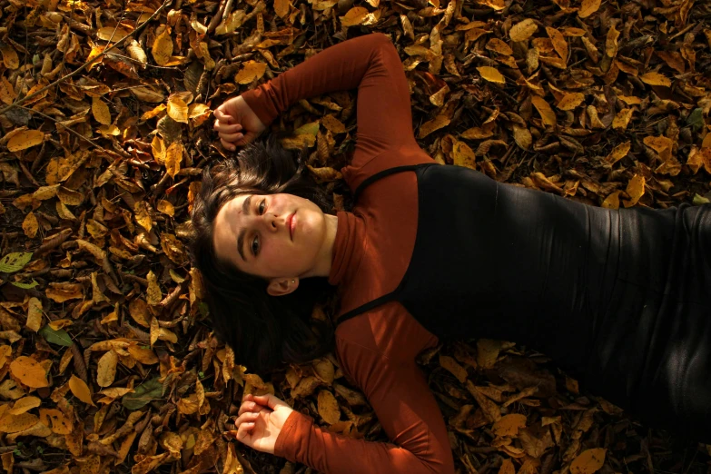 a woman is laying on a bed of fallen leaves