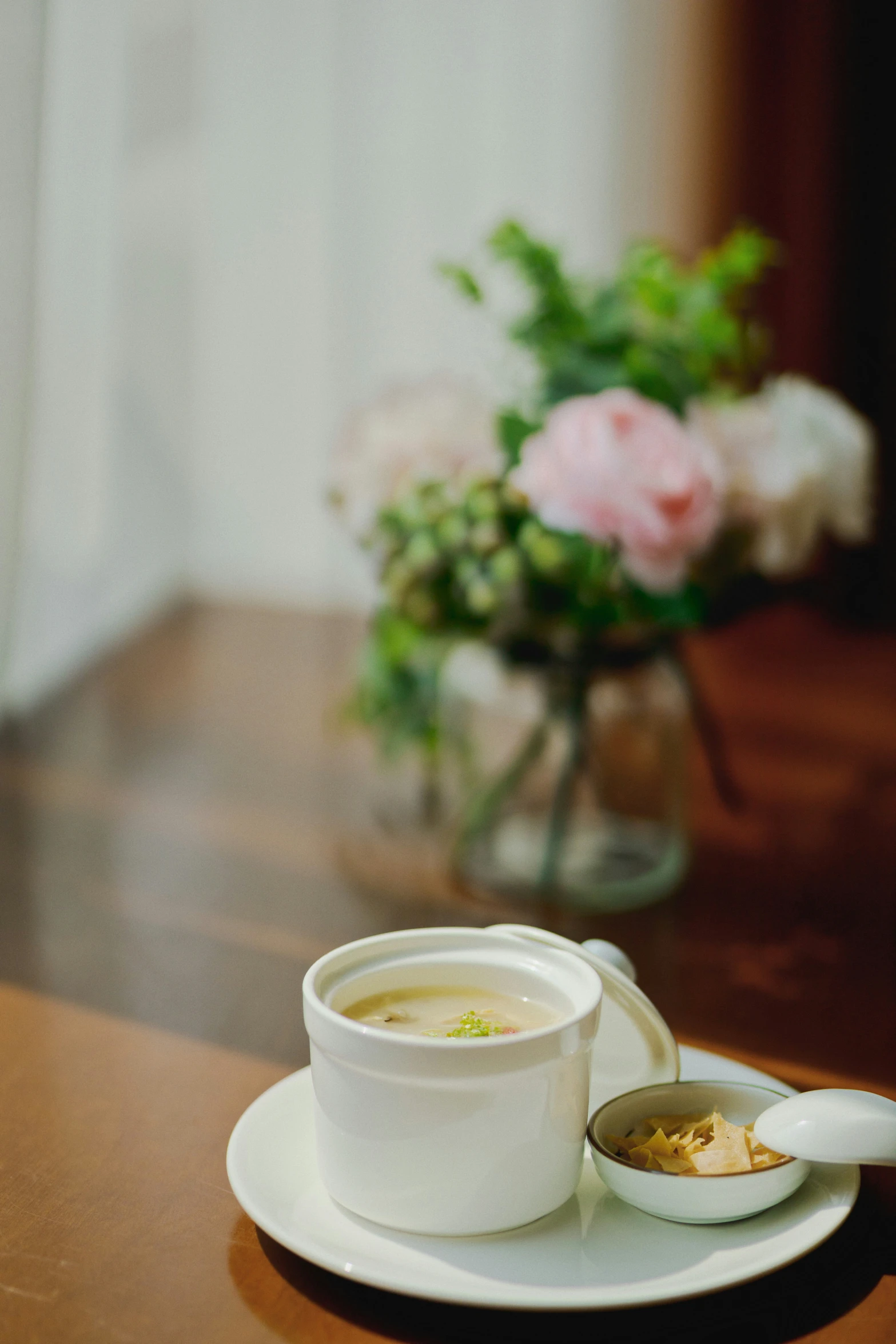 a white saucer filled with soup sits on a table near flowers