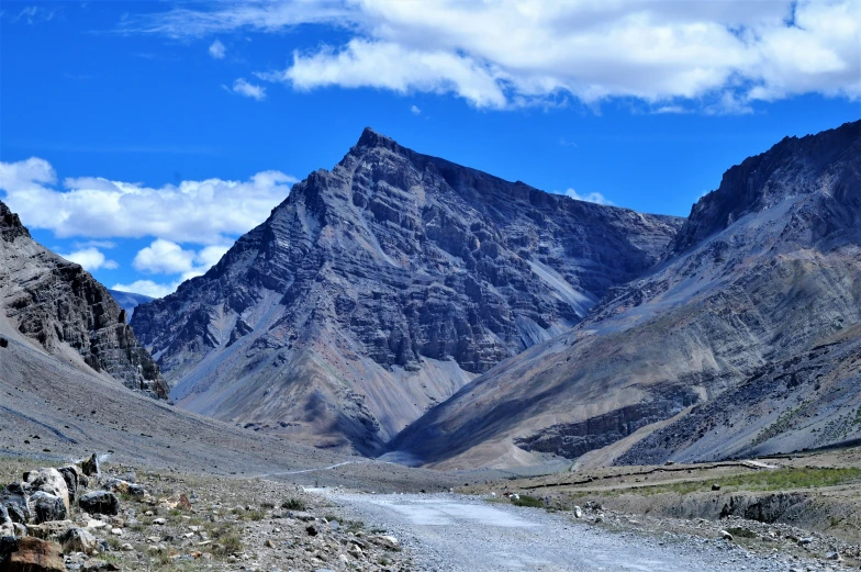 a mountain landscape with a dirt road in the foreground and a blue sky filled with white clouds