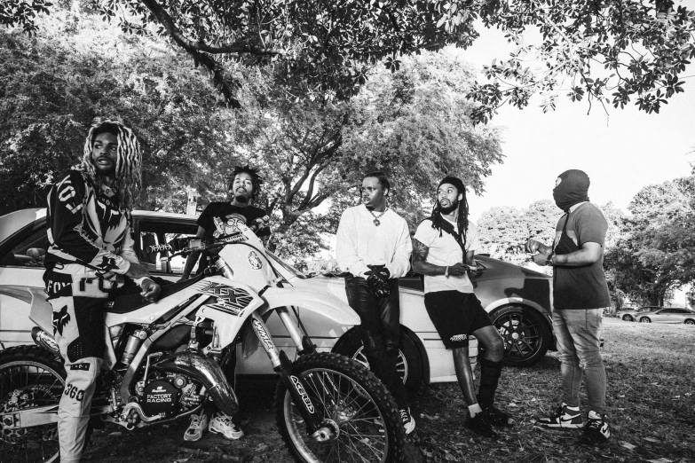 four people stand around one motorcycle while the other sits next to it