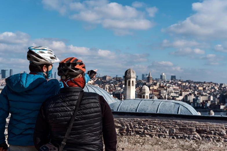 the back of a couple wearing helmets, facing at a view of the city