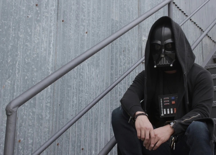 a man in black star wars costume sits on stairs