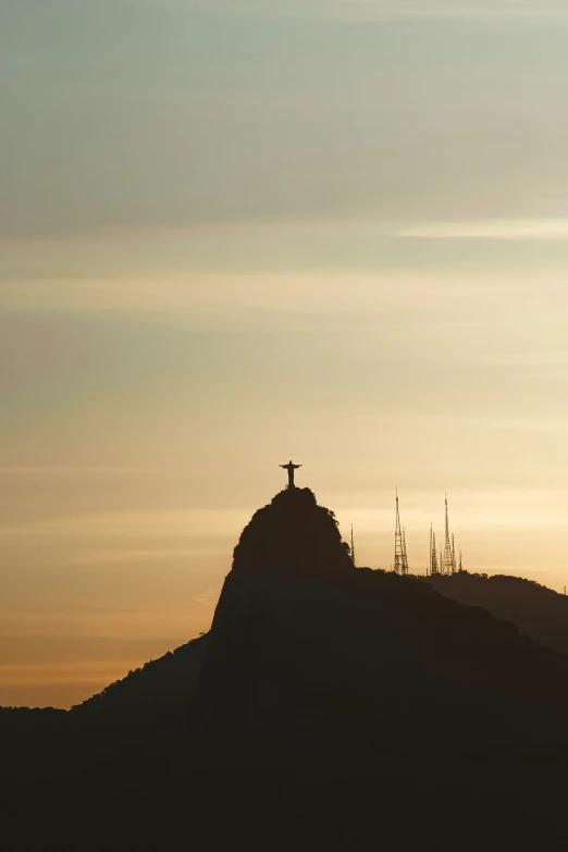 a statue atop a hill at sunset with some clouds in the background