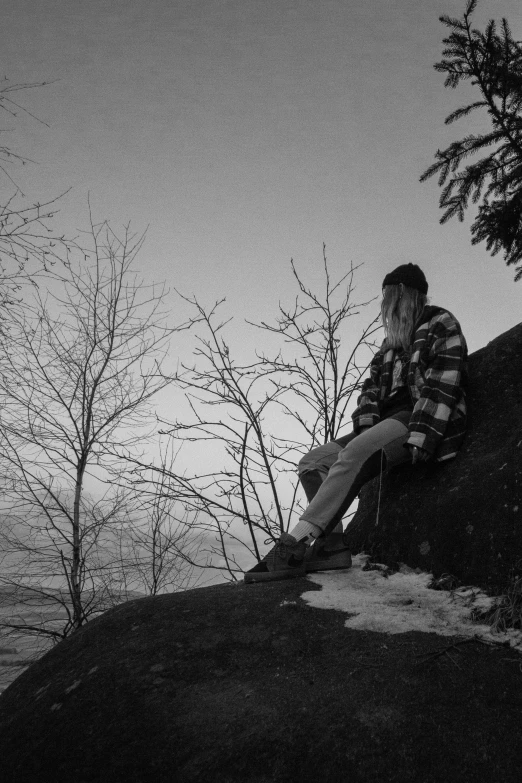 a man sitting on top of a rock next to tree