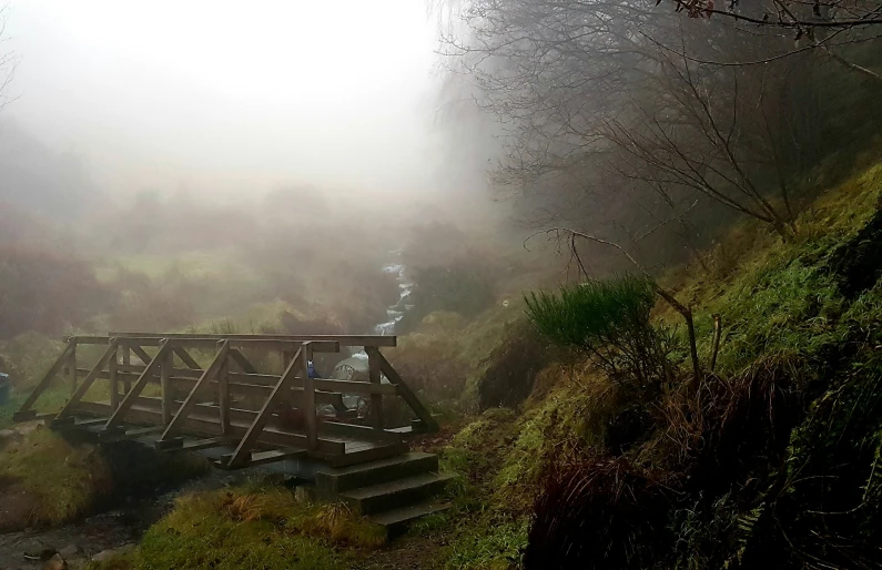 two people hiking through fog by a bridge