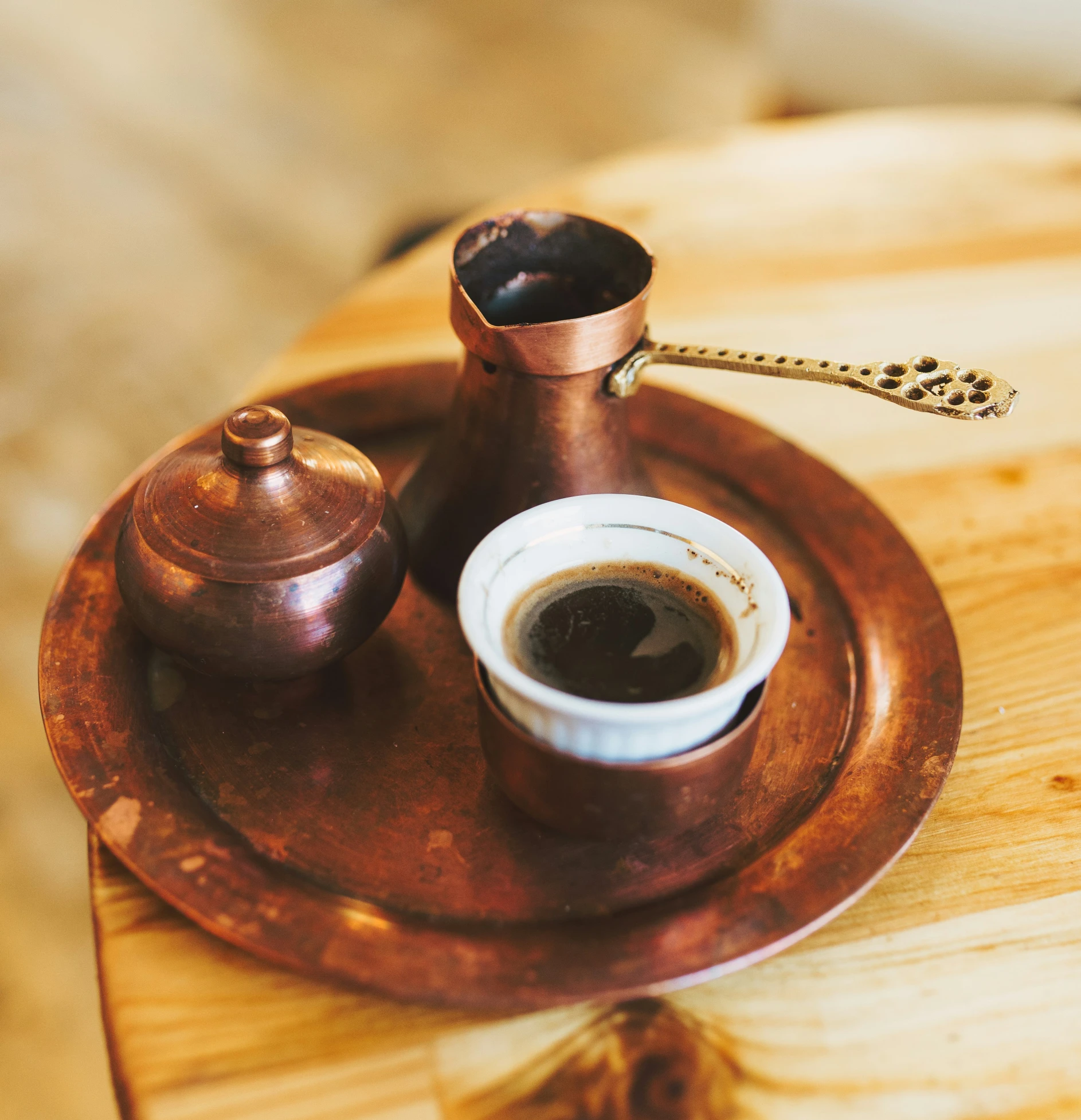 a cup of coffee and a copper saucer on a wooden tray