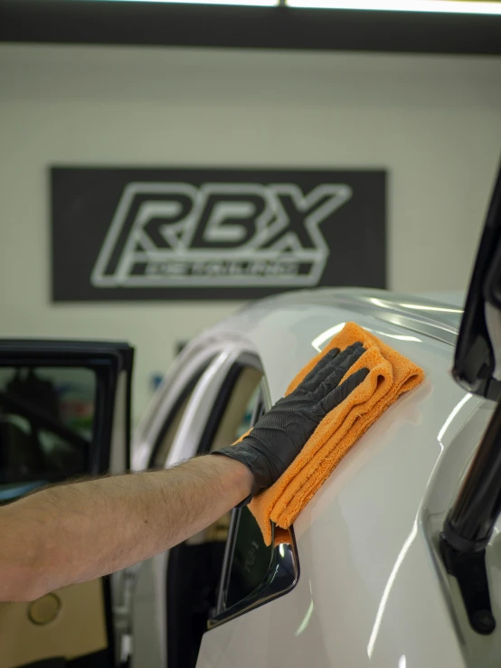 a man polishing the side of a white car with a yellow glove