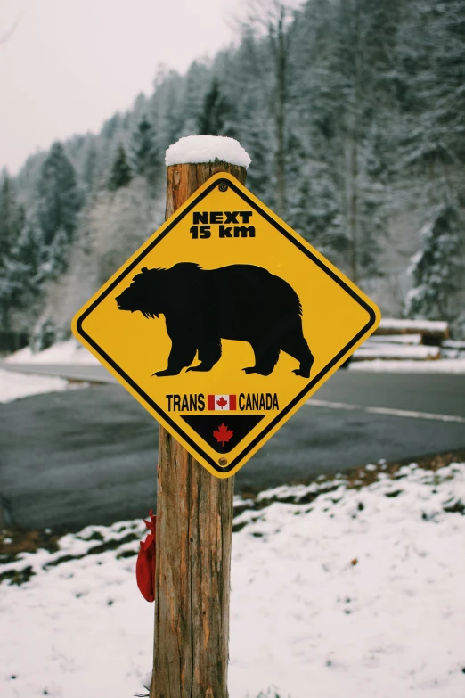 a warning sign on a wooden post with snow