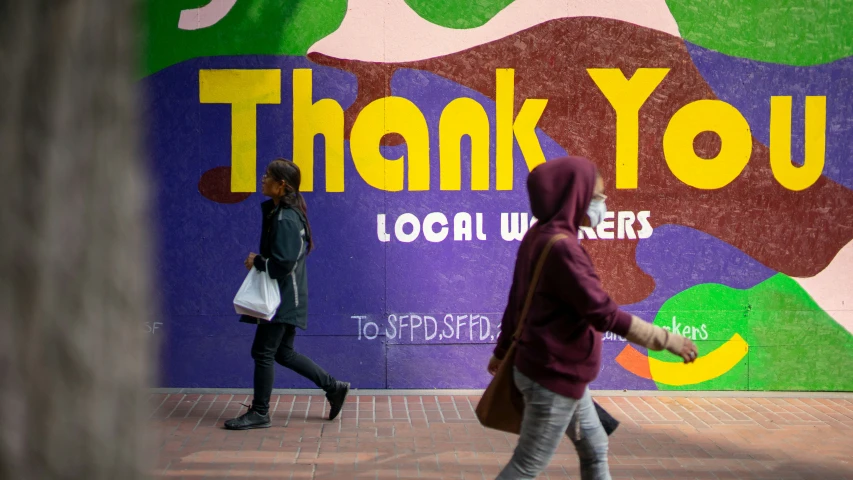 people walking past a thank you mural on a building