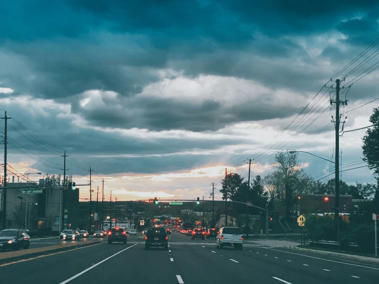 a city street with storm clouds overhead and cars driving down the road