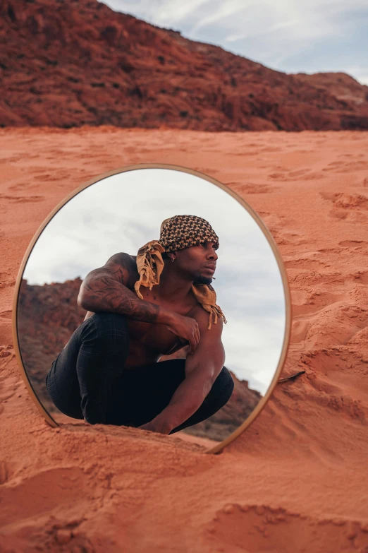 man sits on the beach, while looking at his reflection in the mirror