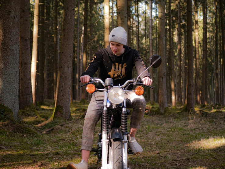 a young man is sitting on a motorcycle in the woods