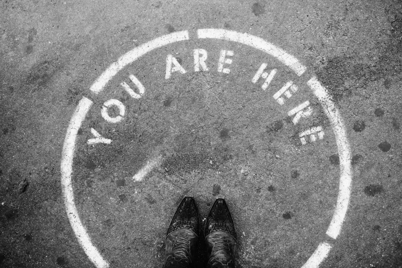 a person is standing next to a parking meter and the words you are here written on the ground