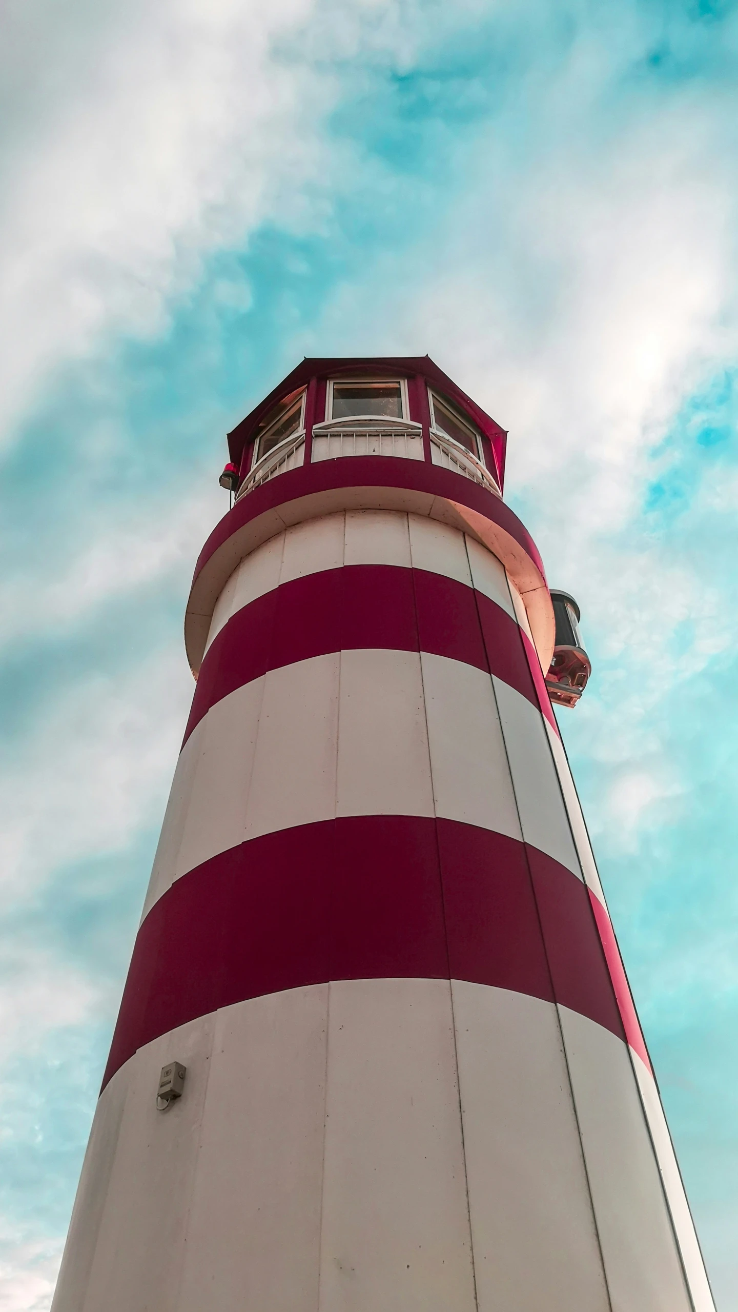 the side of a large red and white lighthouse under a cloudy sky