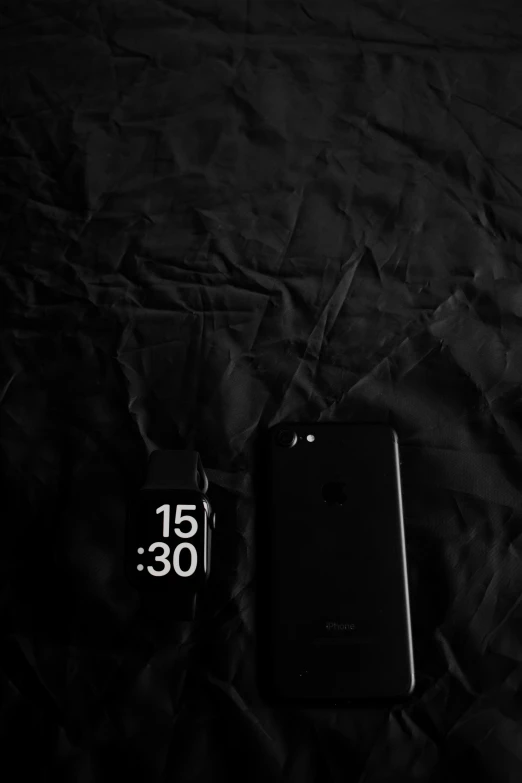 a cell phone next to an alarm clock on a bed