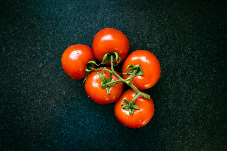 five red tomatoes are on a green surface