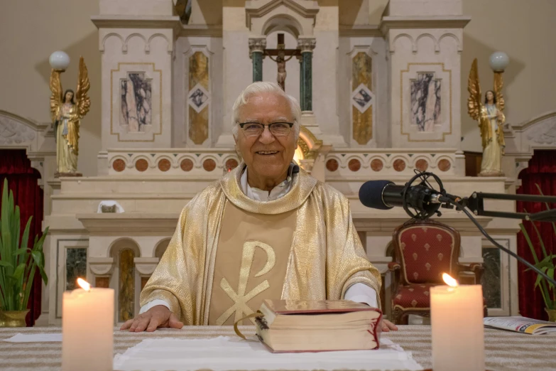 a priest sitting at a table holding a bowl next to candles