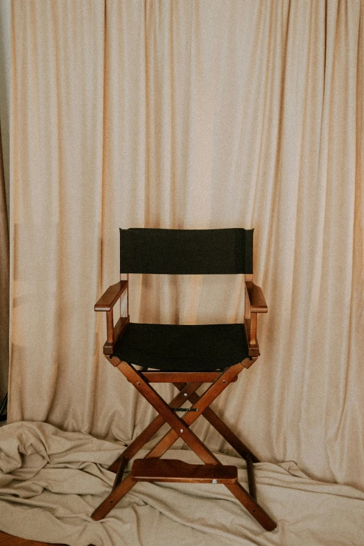 a chair with a wood frame sits on a bed near curtains