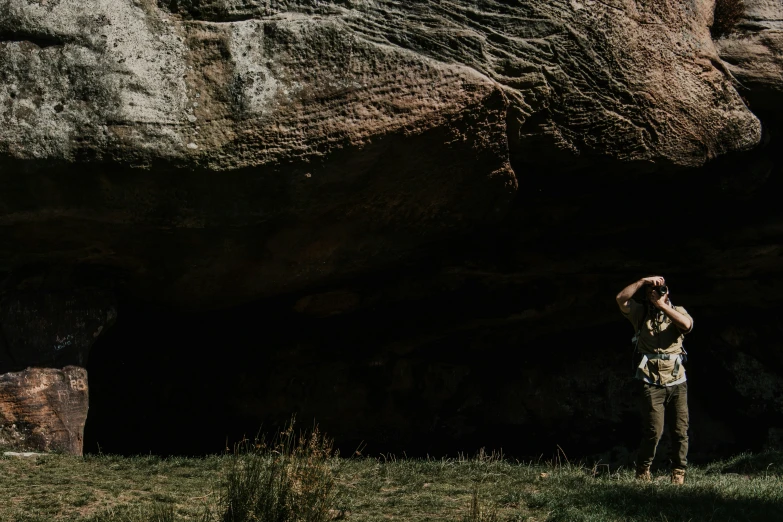 a man standing near a huge rock on a phone