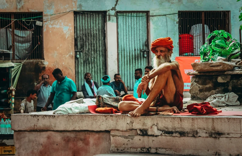 a man in orange turban sits on stone step with people watching him