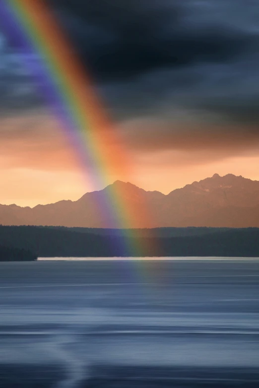 a rainbow is in the dark sky near mountains