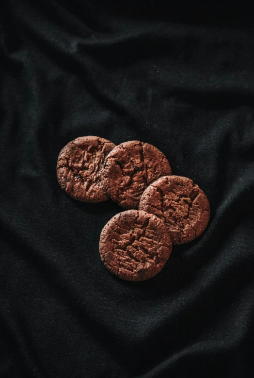 three brown chocolate chip cookies resting on a dark fabric