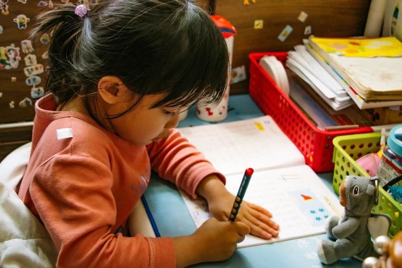 a girl sitting at a desk drawing in a notebook