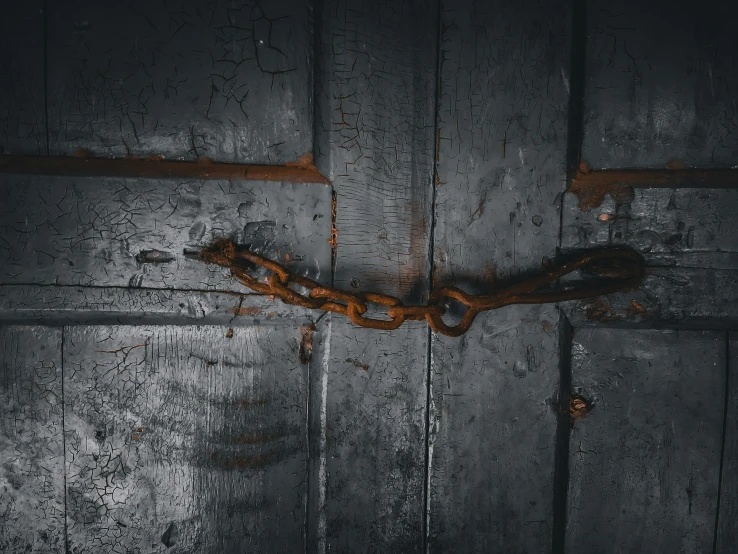 a wooden door with rust on the handle and part of the door chain that is bent upwards in a downward position