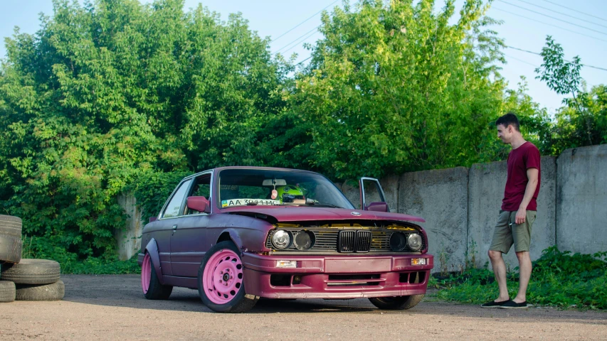 a man standing next to a pink colored car