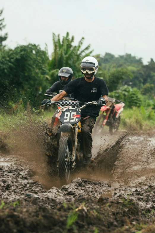 two men on dirt bikes riding through the mud