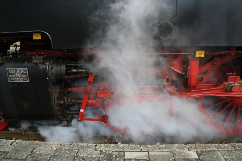 the steam engine is blowing smoke next to the brick wall