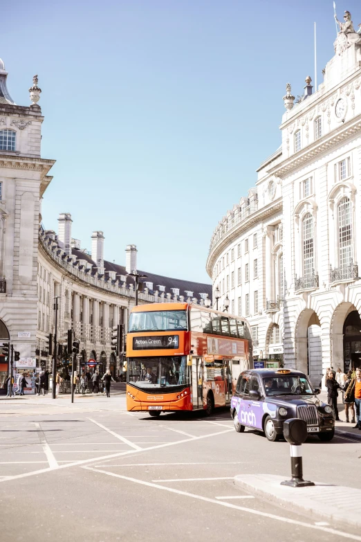 an orange double decker bus drives down the street