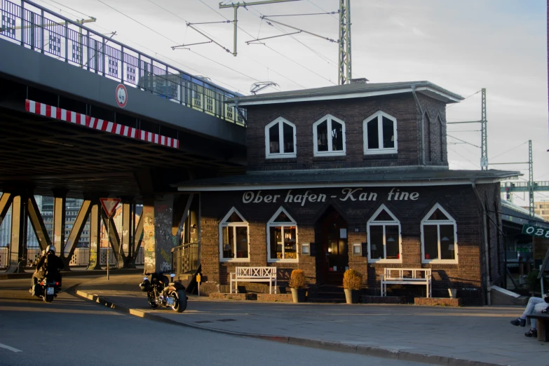 people walk past a bricked building with a bridge over it