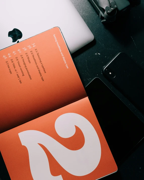 an orange brochure sits next to a laptop