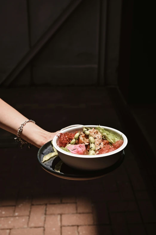 someone holding a bowl filled with food on top of a tray