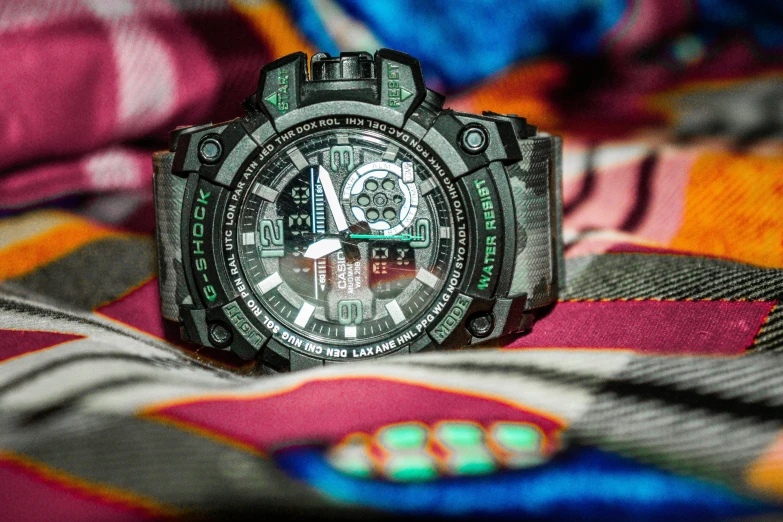 a big dial black watch sitting on top of a colorful cloth