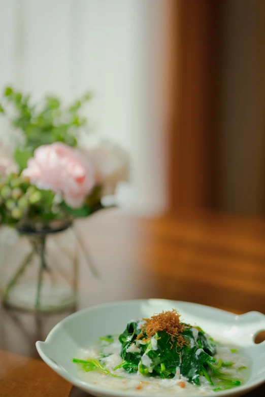 a bowl of soup on a table with some flowers in the vase