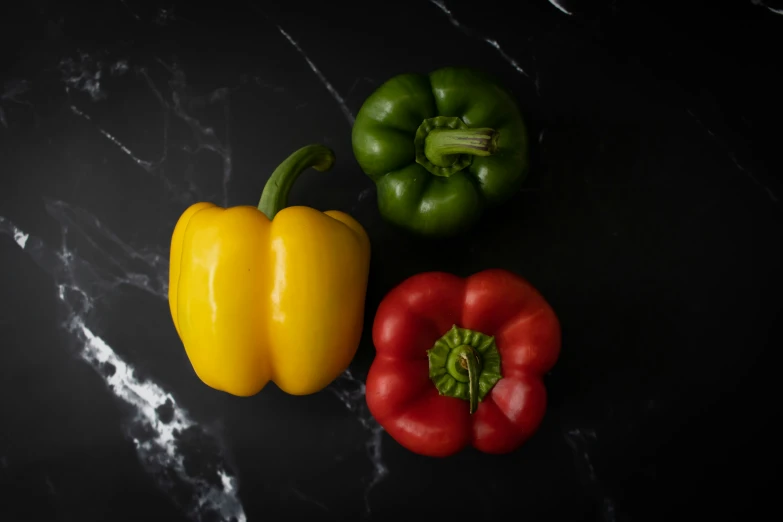 three vegetables on a black table with one yellow pepper