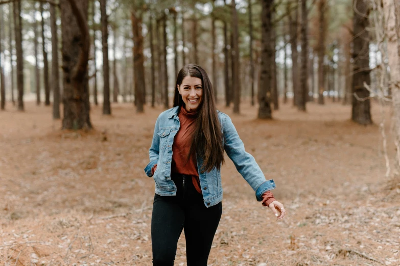 a woman walking through a forest next to tall trees