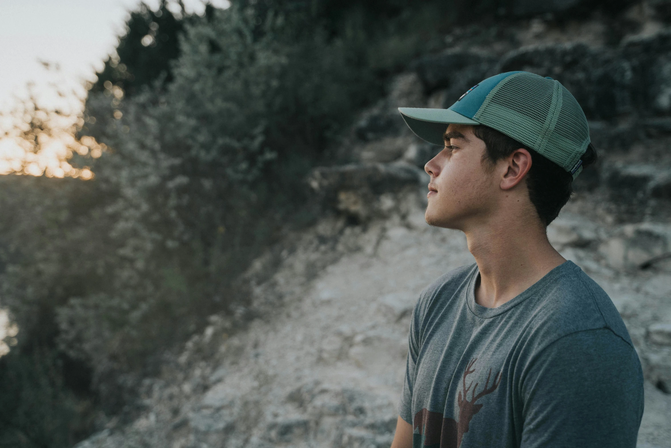 the man with a baseball cap stands on a rocky cliff