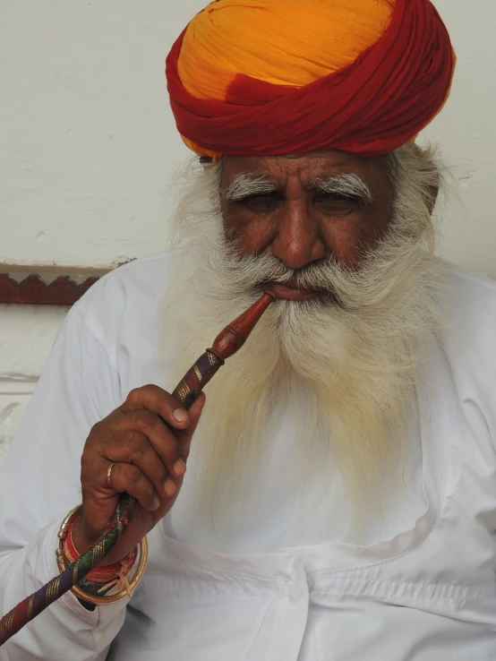 an old man playing the flute while wearing a red turban