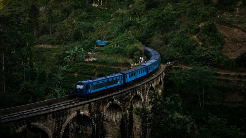 the blue train is driving on tracks along a cliff