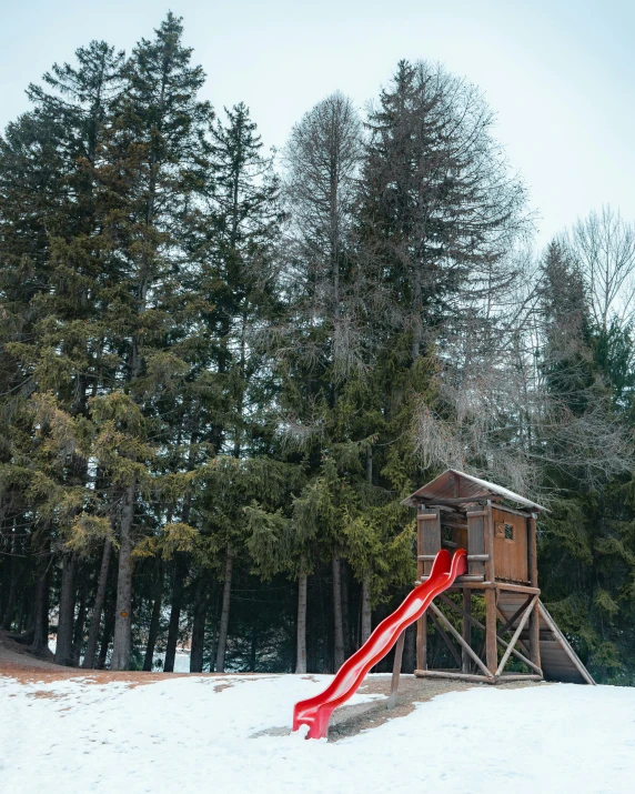 a playground set in the snow with a red slide
