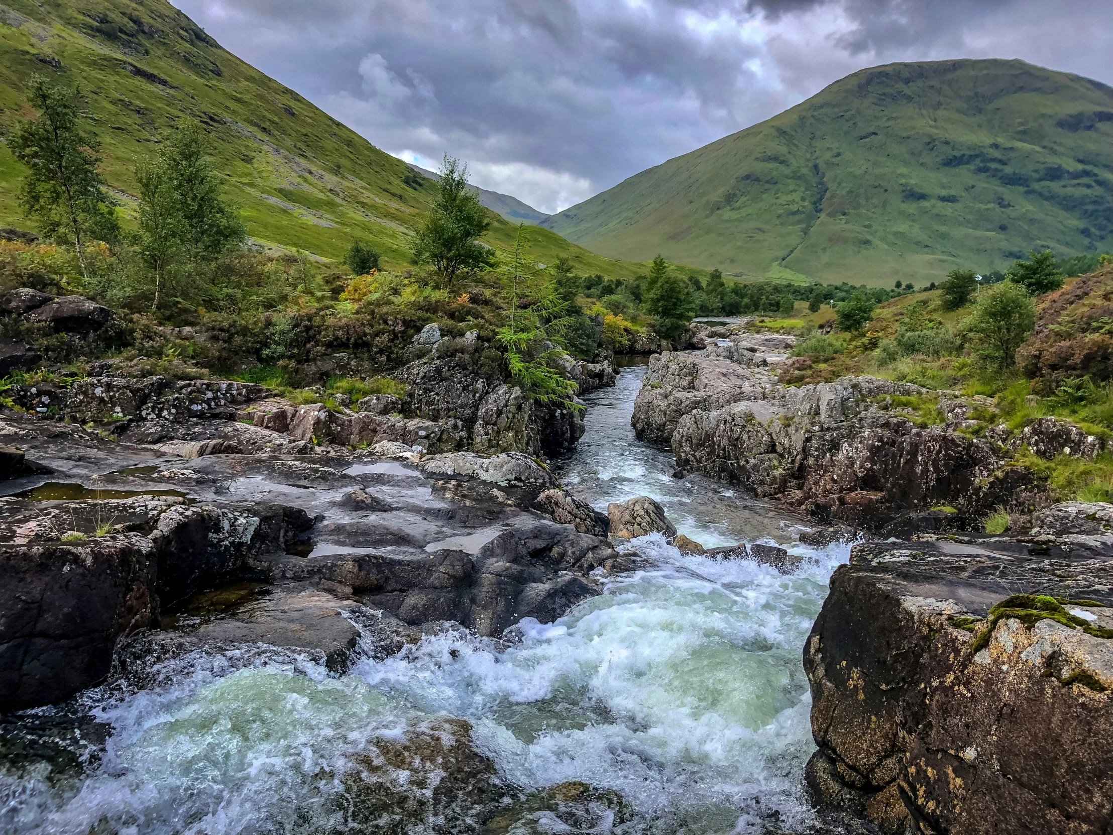 the river flowing through the valley with green mountains in the background