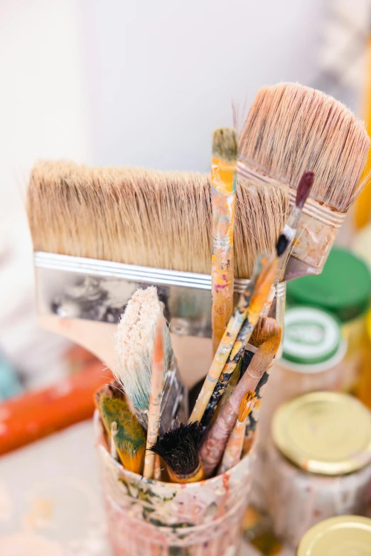 there is lots of paint brushes in a glass with cups on the table