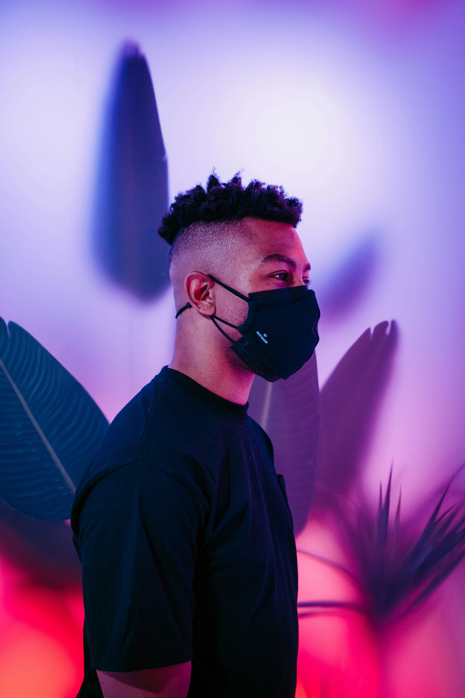 a man in a face mask with palm leaves on the wall behind him