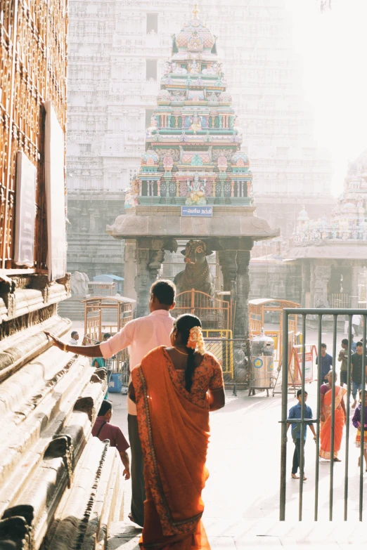 an indian man and woman in orange sari pointing to the temple